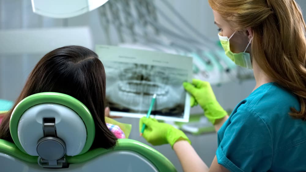 Stomatologist showing female teeth x-ray image, cavities, periodontal disease